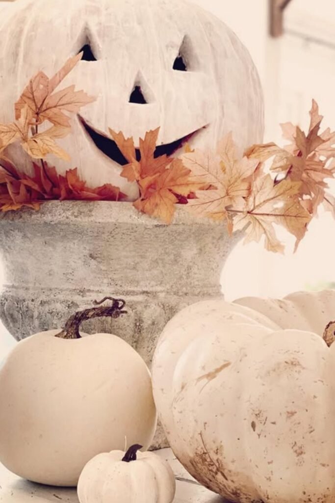 White pumpkins styled with a carved jack-o'-lantern and autumn leaves on a cozy porch corner.