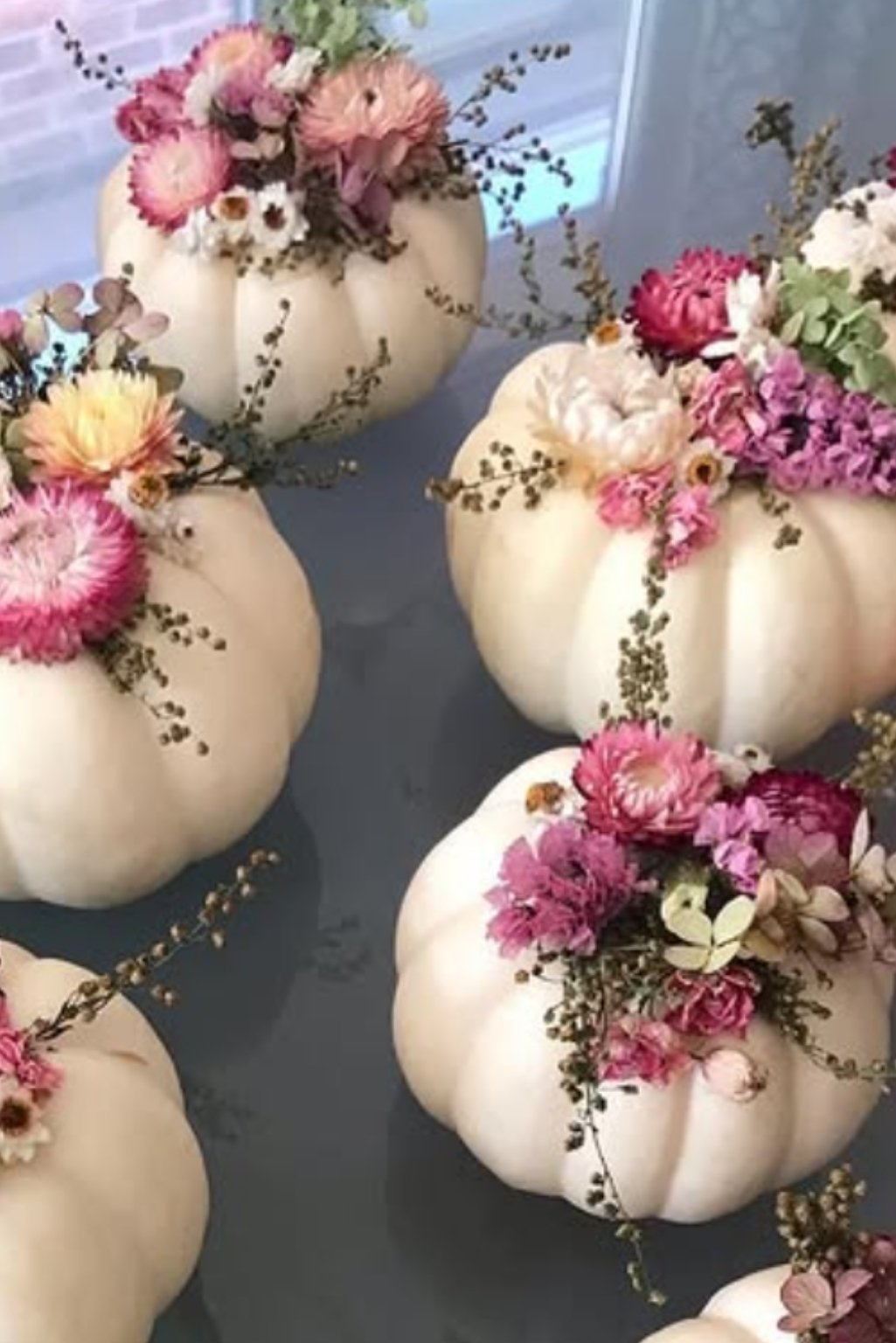 White pumpkins decorated with pink and berry-toned flowers for a romantic fall centerpiece.
