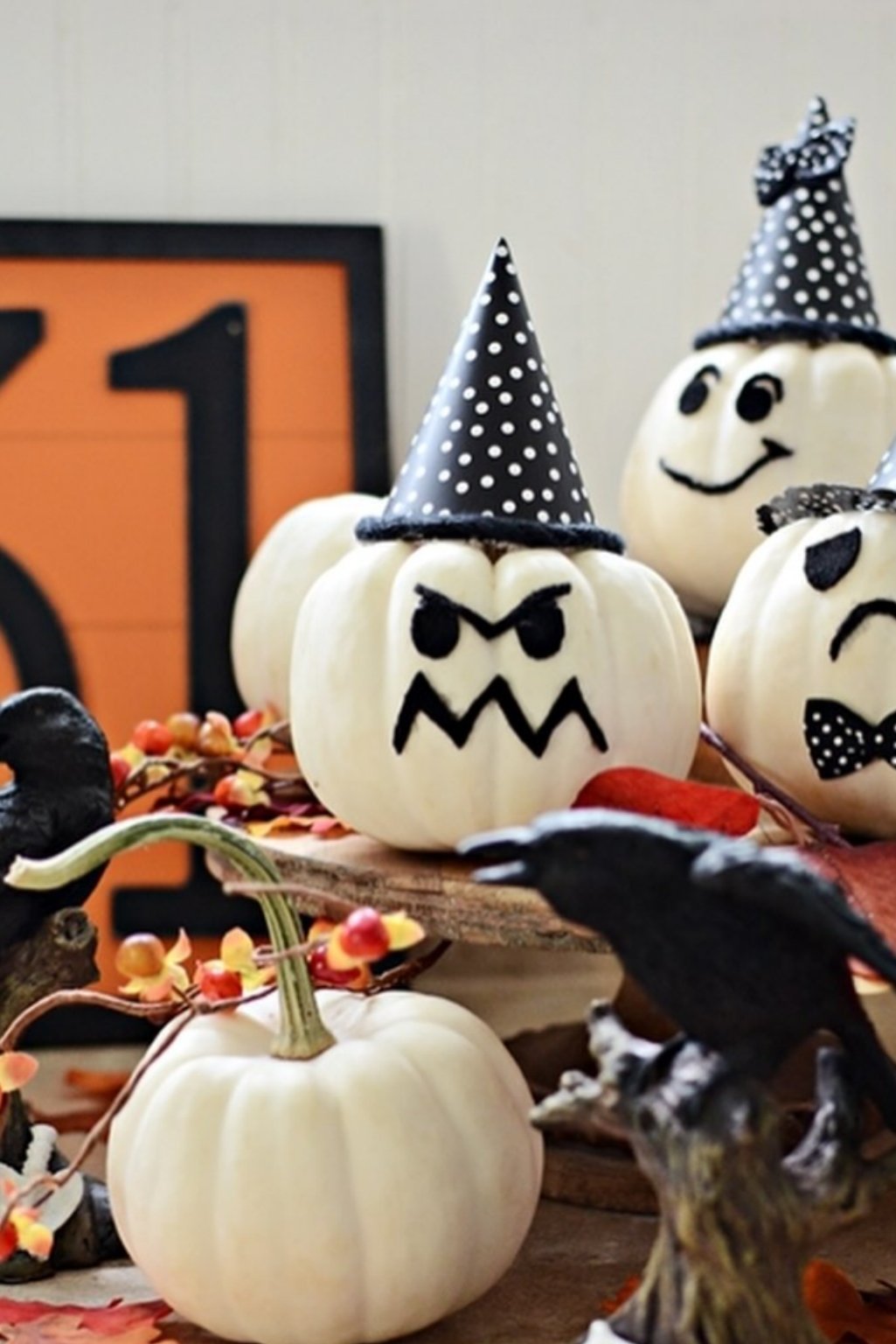 Halloween-themed white pumpkins painted with expressive black faces and party hats.