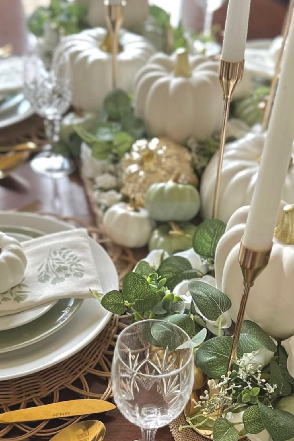 Elegant fall table setup with taper candles, eucalyptus, and layered white pumpkins.