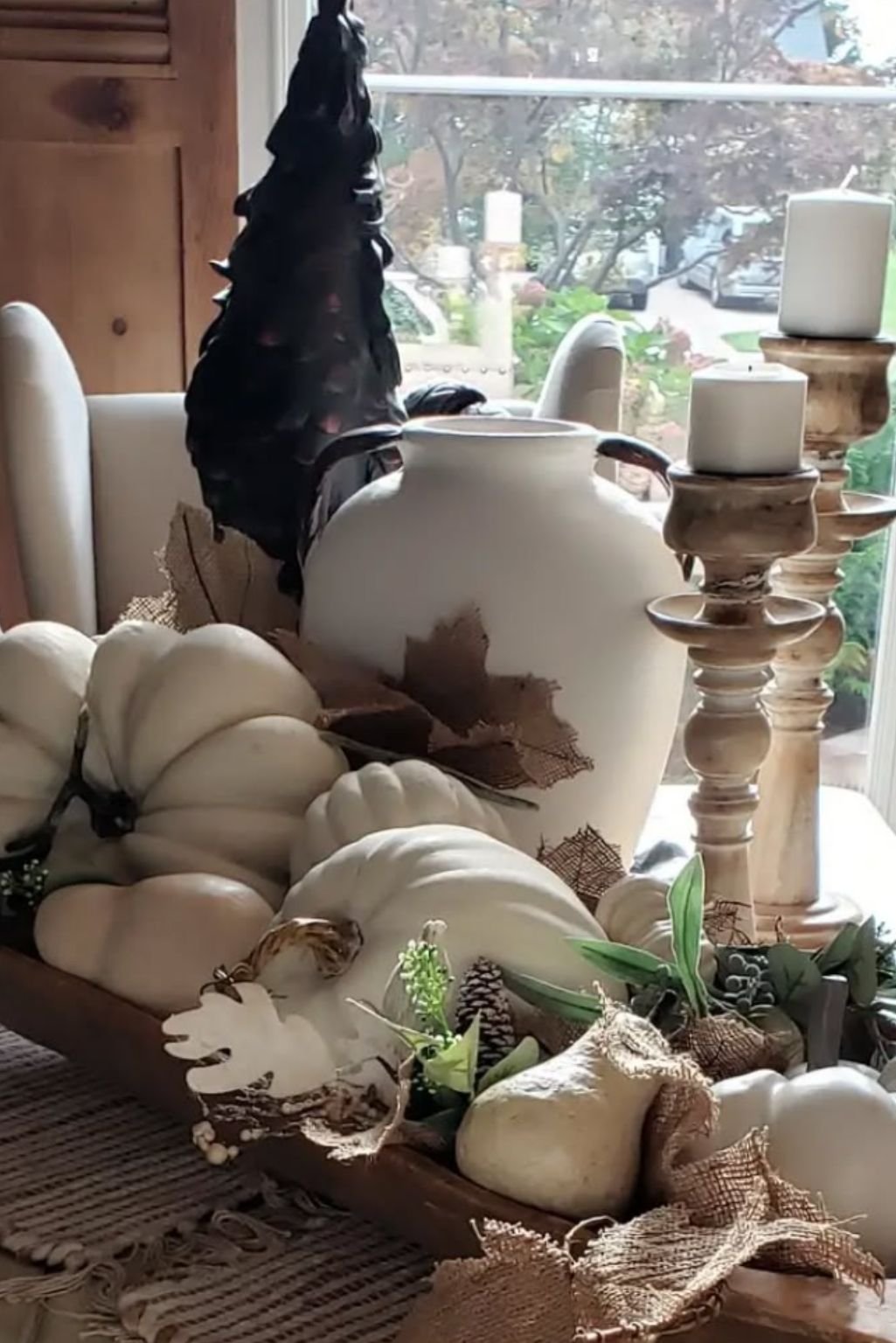 Natural-toned vignette with white pumpkins, ceramic vases, and wooden candle holders.