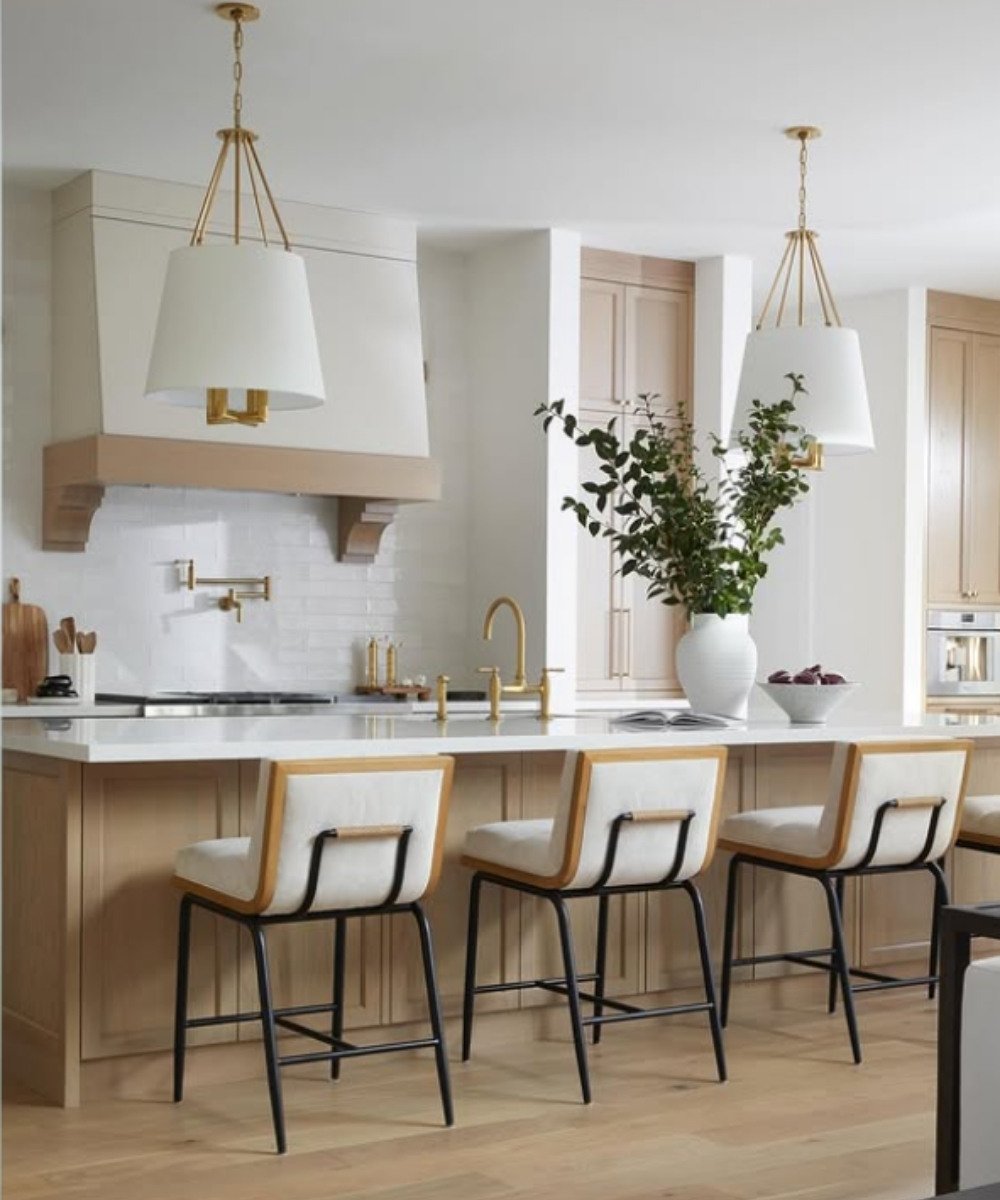 Modern white kitchen with light wood island, gold fixtures, and white upholstered bar stools