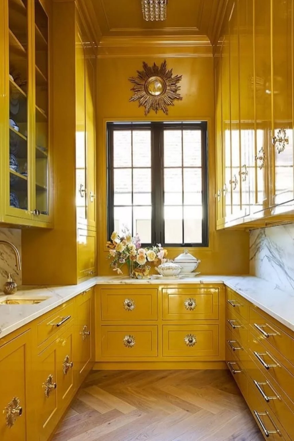 High-gloss yellow kitchen cabinets with ornate sunburst knobs and marble counter