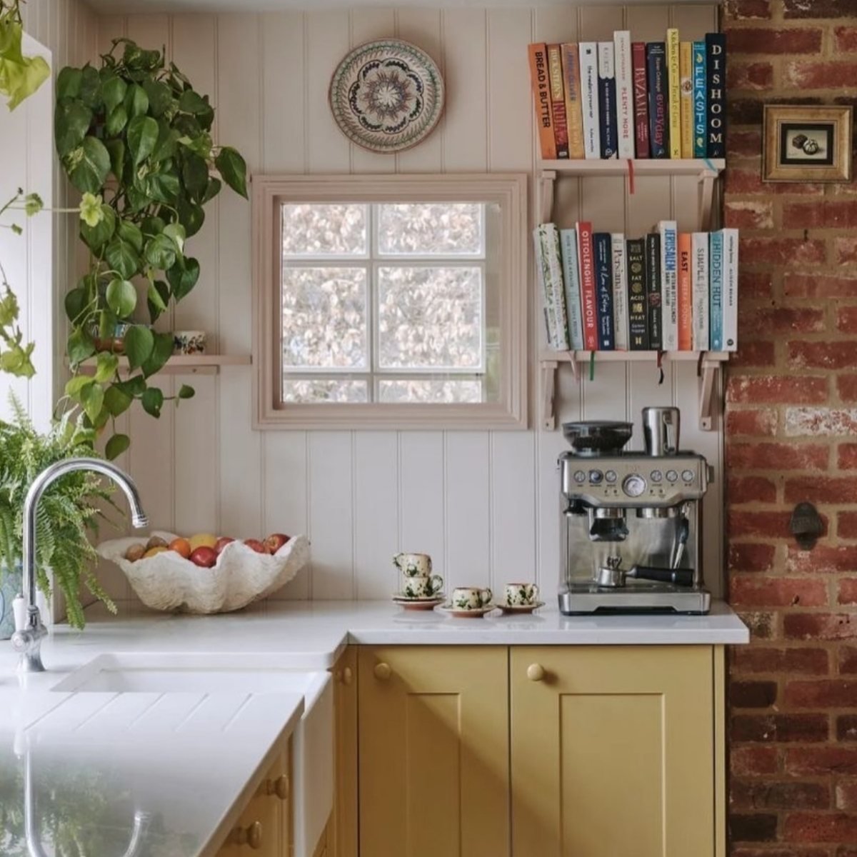Yellow base cabinets in a kitchen corner with red brick wall and books
