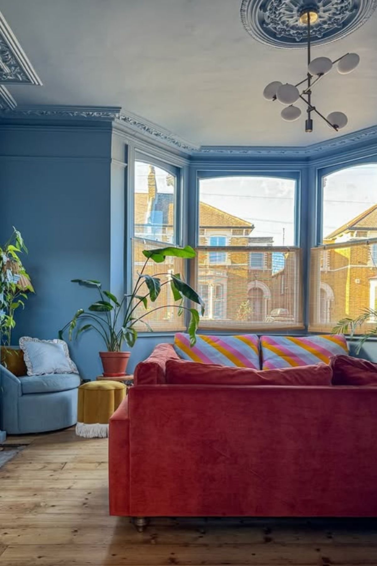 Rust-red sofa with striped cushions in sunny bay window against light blue wall paint color.