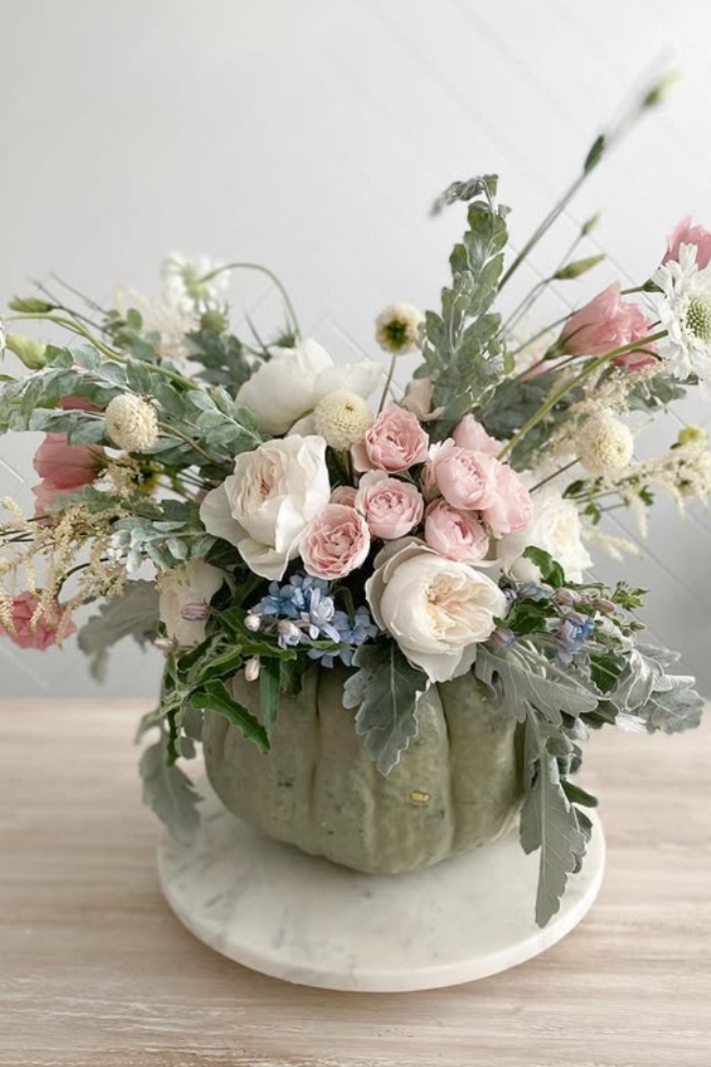 Soft pastel pumpkin floral arrangements with pale roses, eucalyptus, and delicate fillers in a green pumpkin.