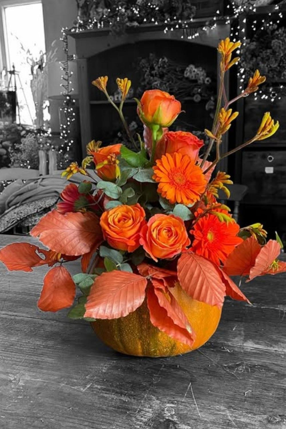 Bold orange pumpkin floral arrangements filled with roses, gerbera daisies, and autumn leaves.