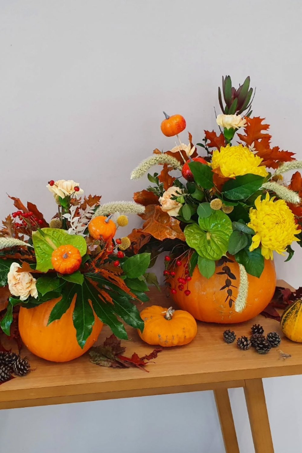 Bright floral arrangements in pumpkins with yellow chrysanthemums, red berries, autumn leaves, and seasonal greenery.