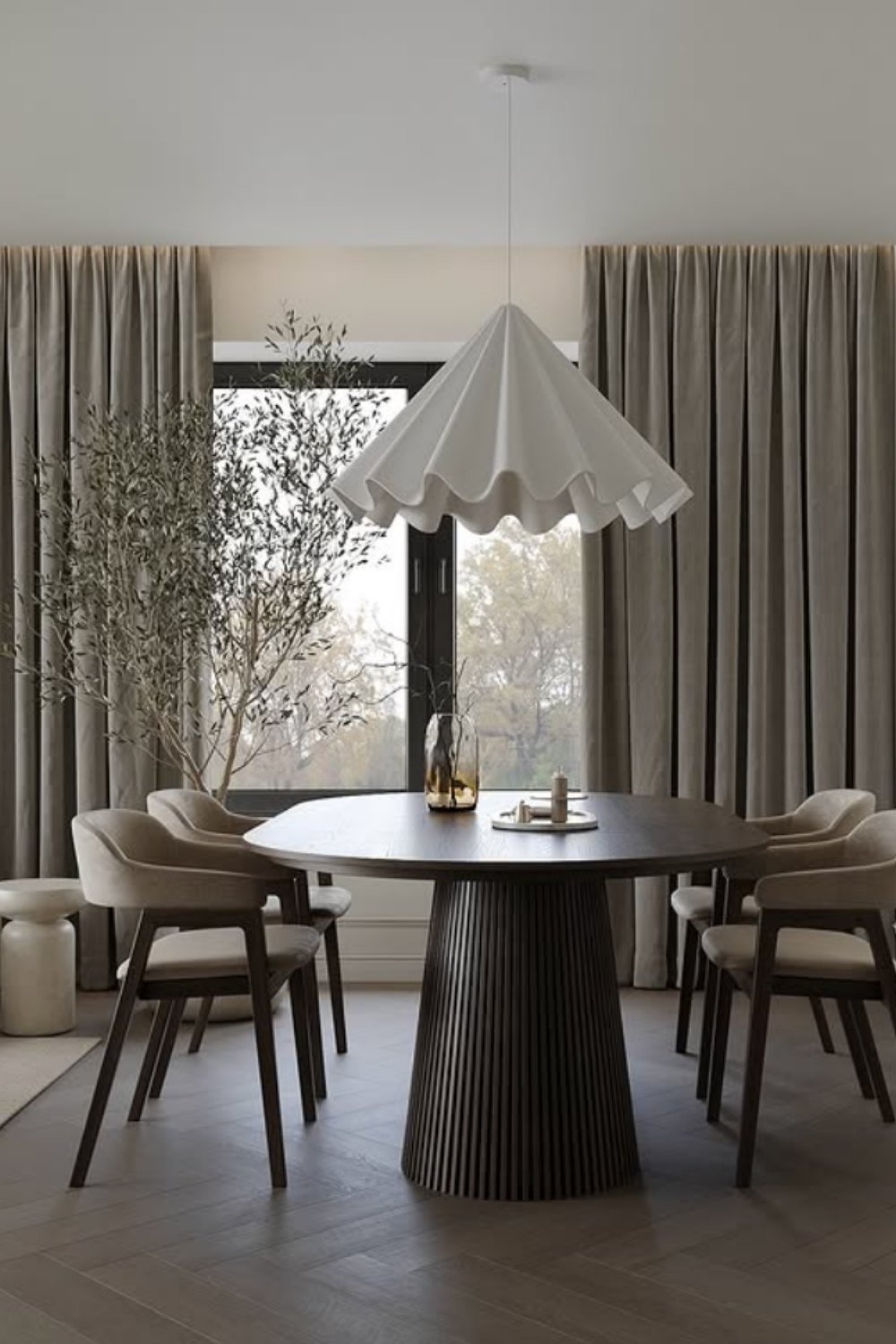 Neutral dining room with sculptural pendant, round dark table, and soft curtains.