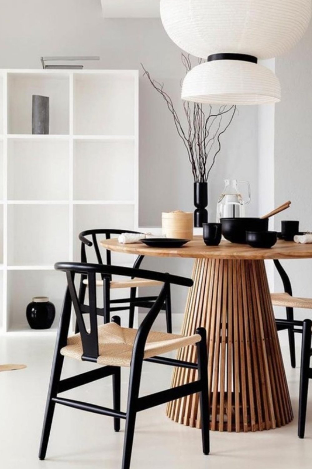 Dining space with sculptural wood table base and black chairs in neutral room.