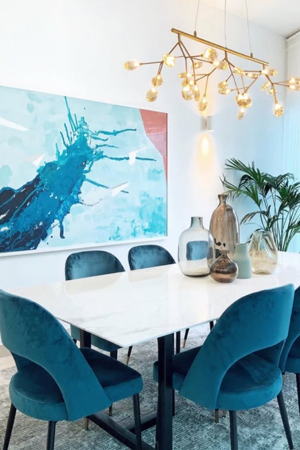 Modern dining room with soft blue chairs, abstract wall art, and gold chandelier.
