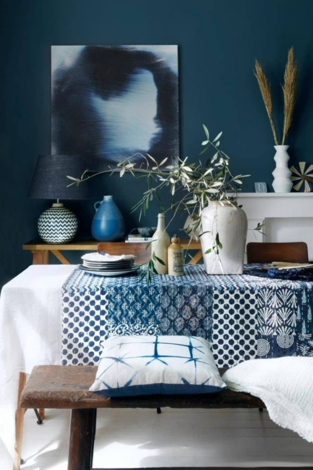 Cozy blue dining nook with patterned textiles, pottery, and olive branch decor against a deep blue wall.