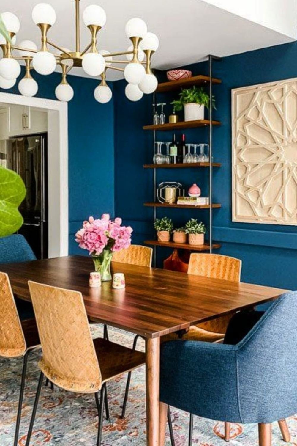 Modern glam dining room with blue velvet chairs, glass table, and metallic chandelier.