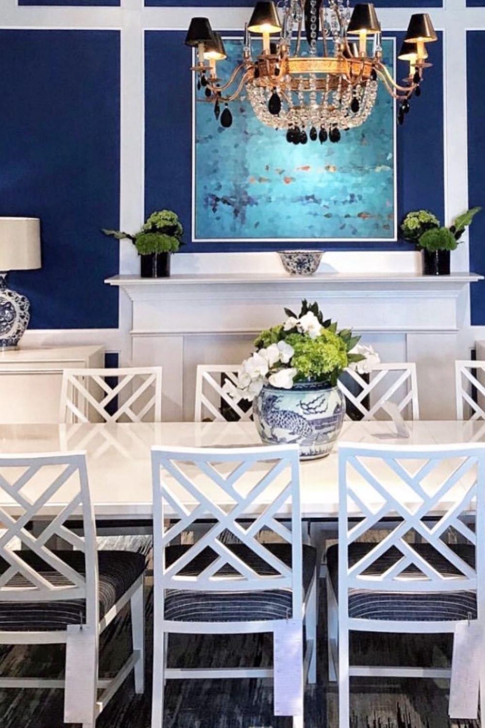 Navy dining room with white chairs and elegant chandelier over a fireplace.