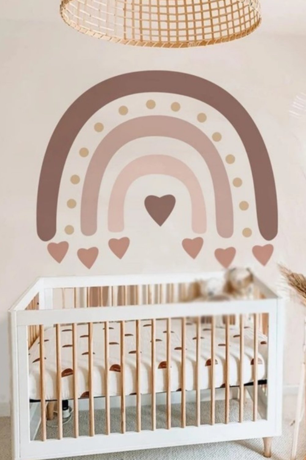 Neutral boho nursery wall with painted rainbow mural and wooden crib.