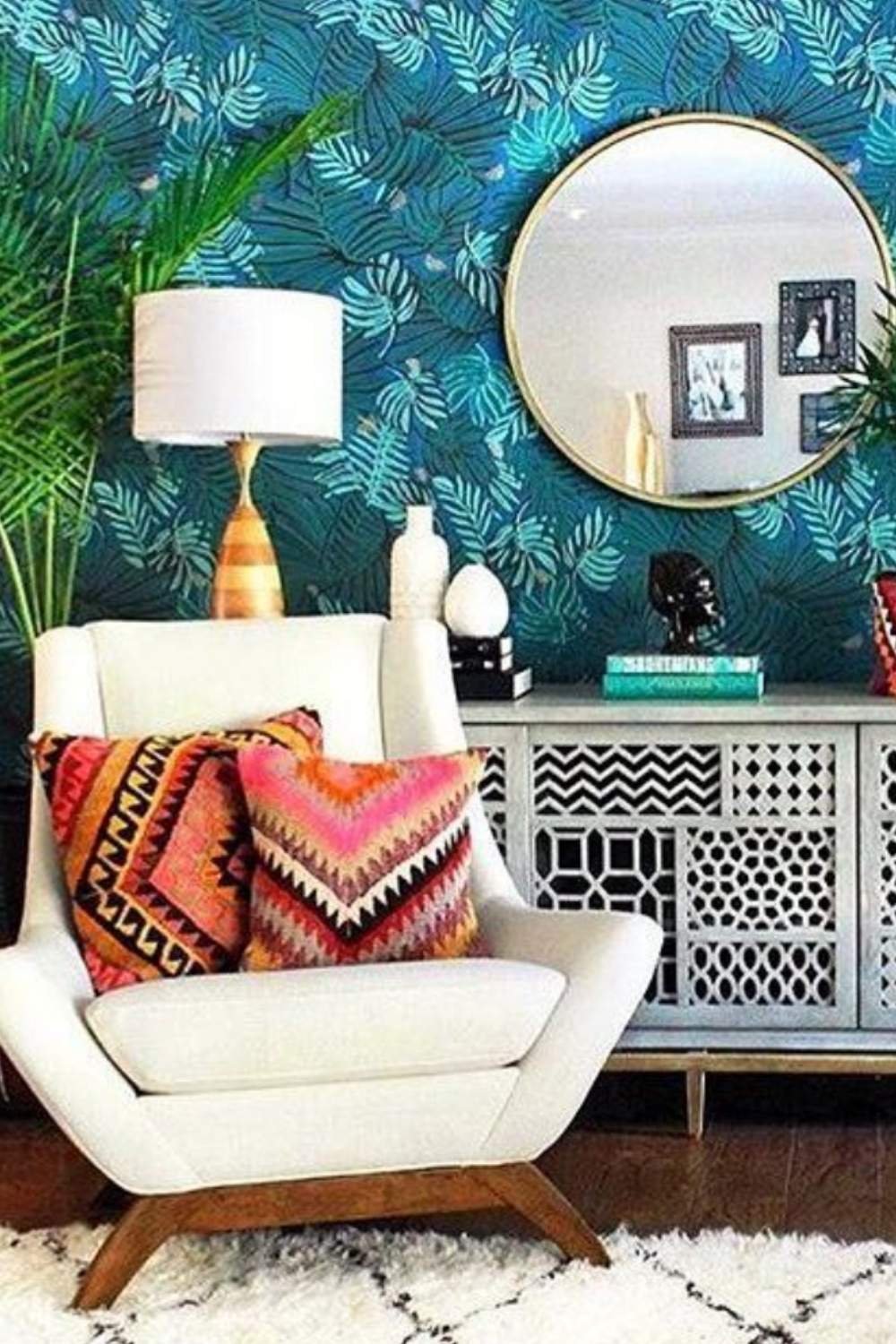 Boho living room wall with teal palm-leaf wallpaper, round mirror, and woven accents.