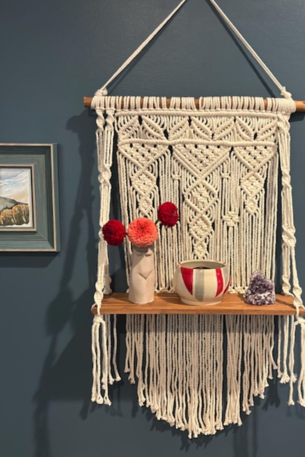 Boho wall with macramé shelf, decorative vase, and dark painted backdrop.