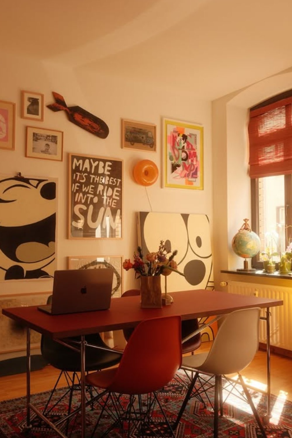 Dining room with sunlit gallery wall featuring playful prints and pops of red.