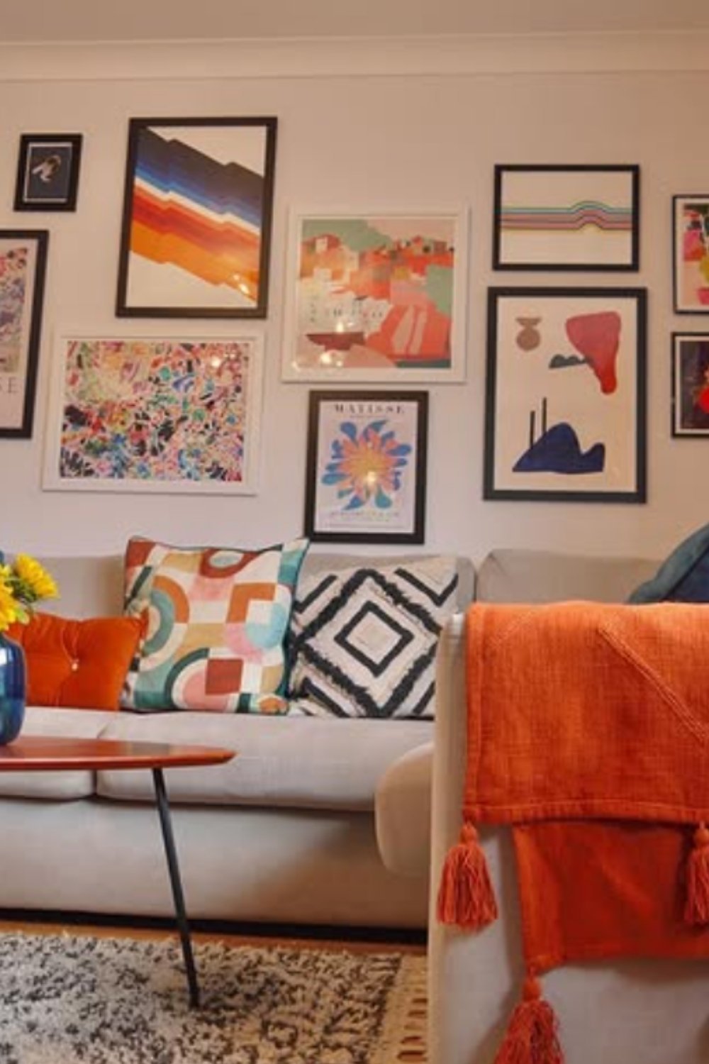Cheerful gallery wall with pastel artwork and cozy textiles in a living room.