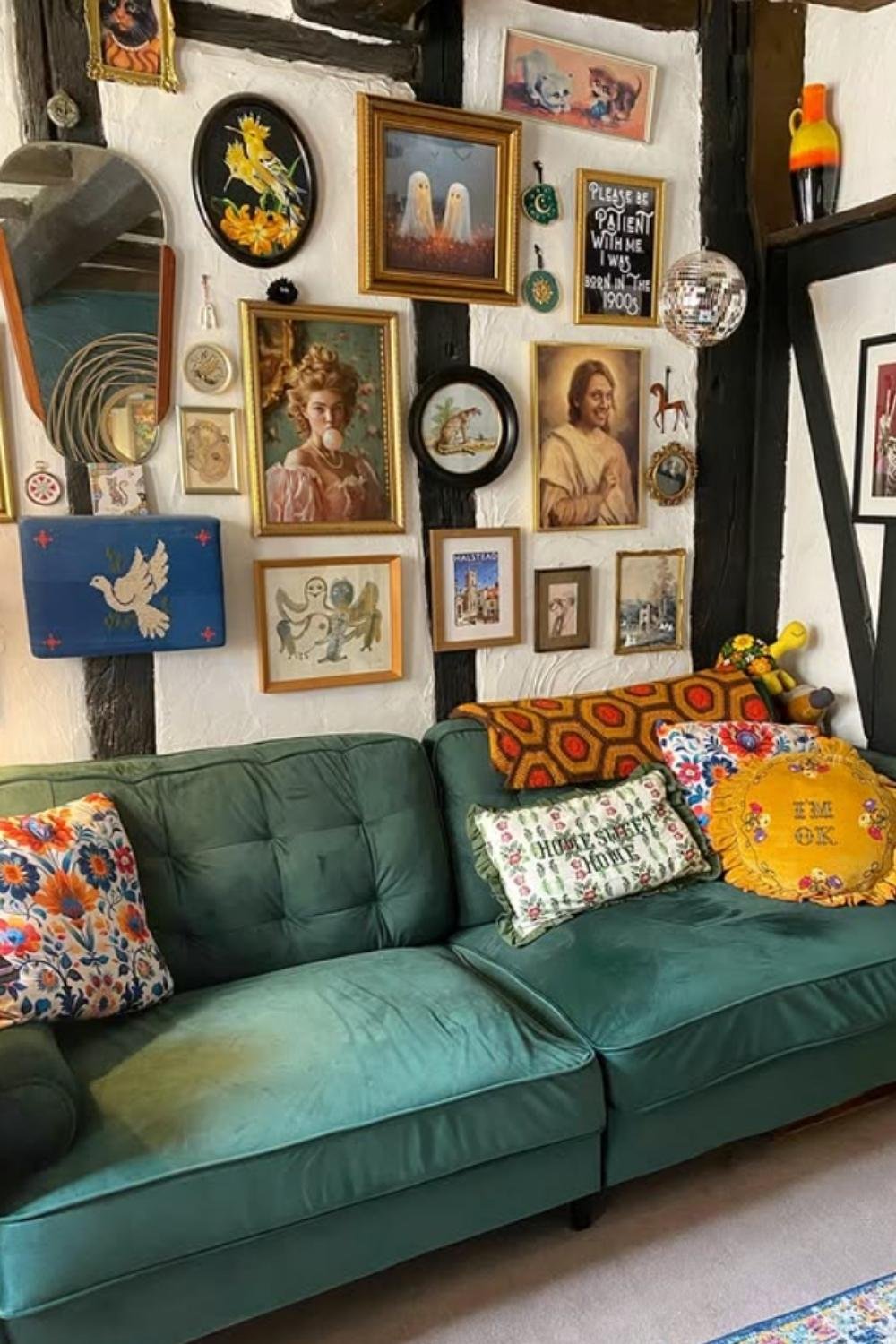 Vintage-style gallery wall with portraits, antique objects, and a green velvet sofa.