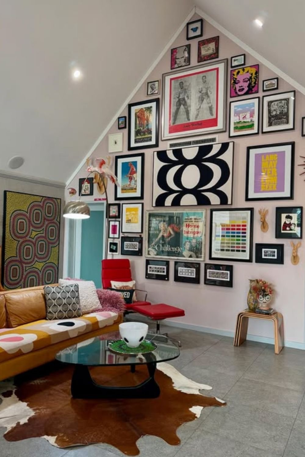 Dramatic eclectic gallery wall on a tall ceiling with oversized central artwork and smaller surrounding pieces.
