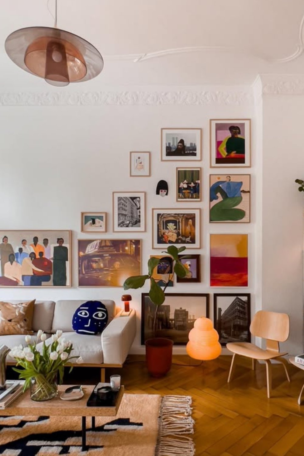 Casual gallery wall with colorful art above a sofa in a parquet-floored living room.