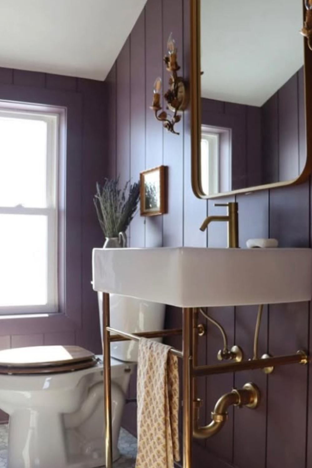 Cozy bathroom with deep purple paneled walls, brass fixtures, and natural light showcasing purple bathroom ideas.