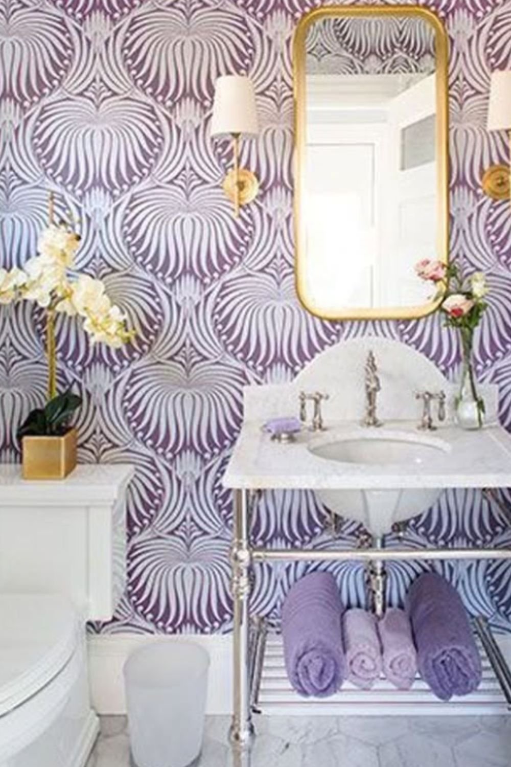 Playful bathroom with purple patterned wallpaper, gold-framed mirror, and coordinated lavender accessories.
