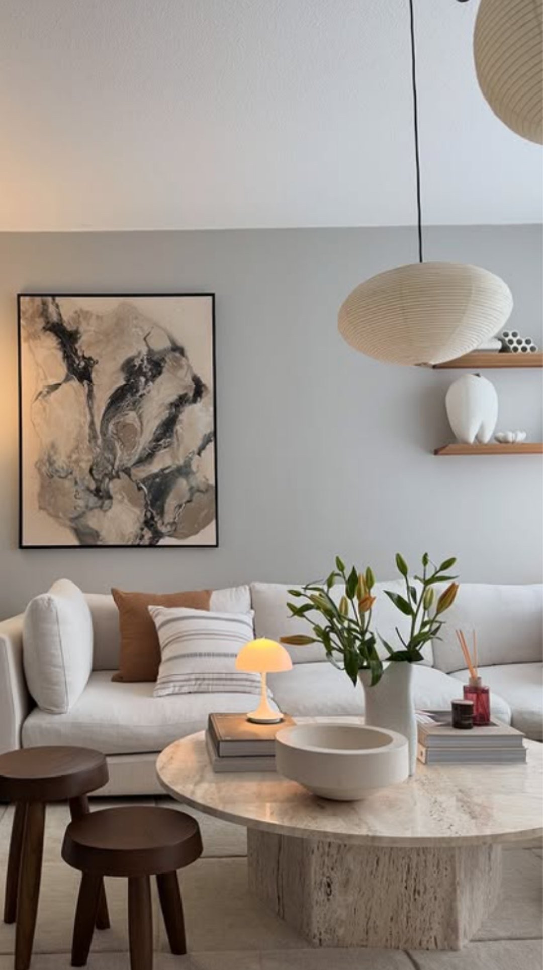 Japandi style living room with a stone coffee table, soft neutral sofa, wooden stools, and modern pendant light.