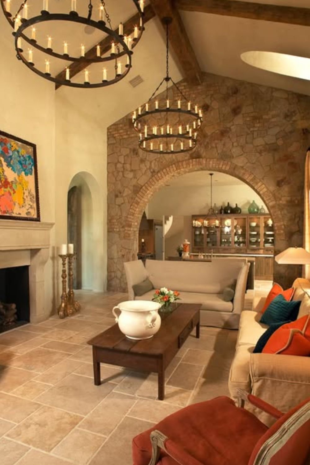 Warm living room with stone walls, arched doorway, and rustic chandeliers