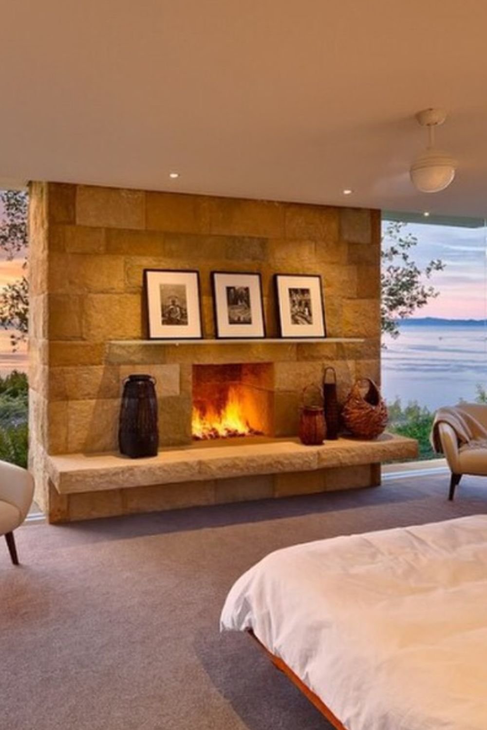Bedroom with stone fireplace, cozy seating, and large window view