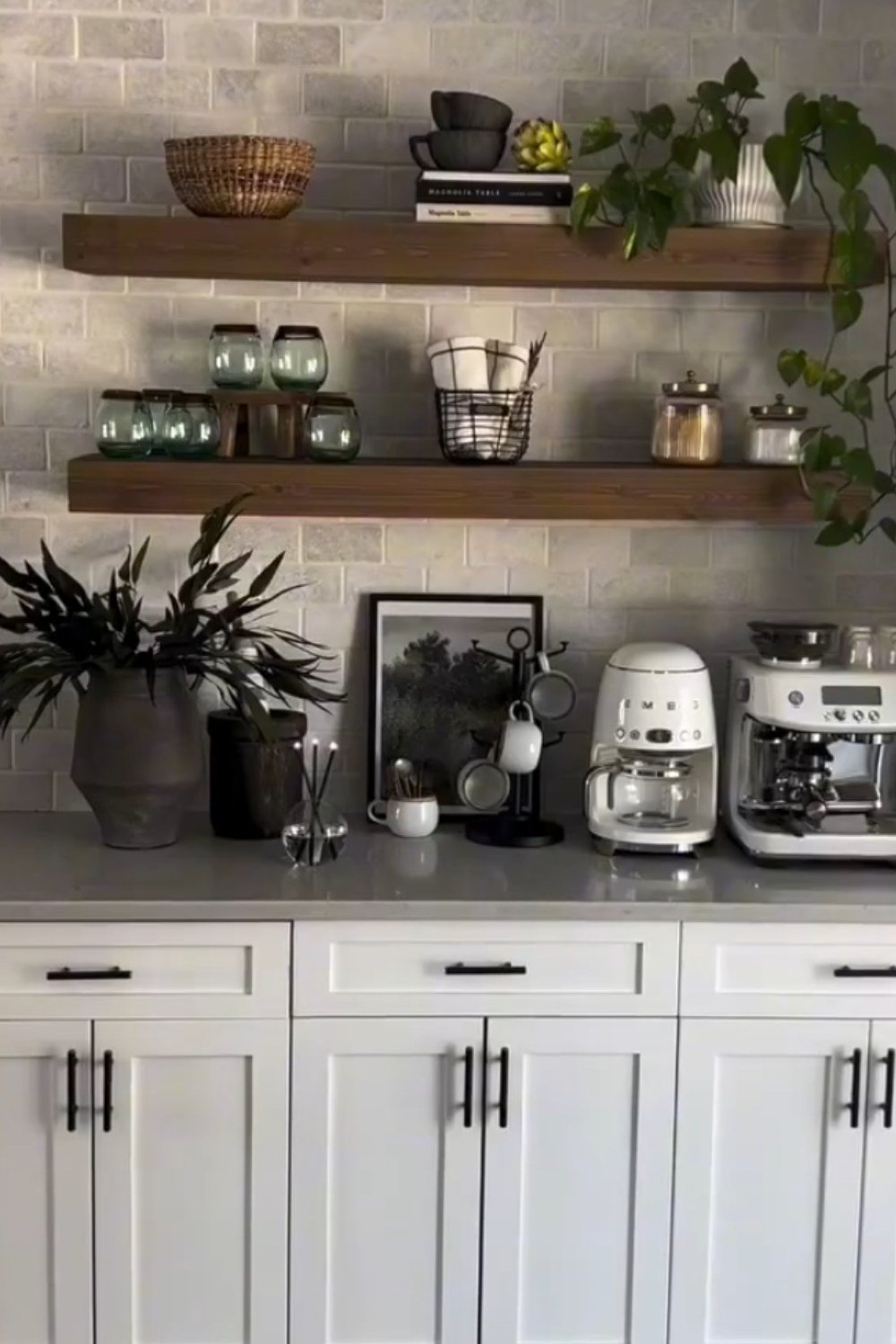 White coffee bar with floating wooden shelves, greenery, and stainless coffee machine.
