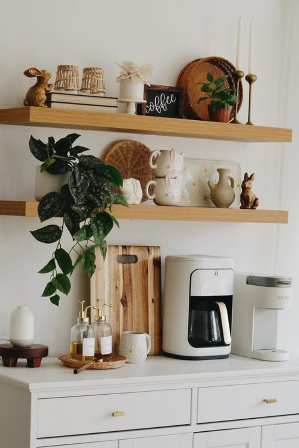 White coffee station with open shelves, plants, baskets, and cutting boards.