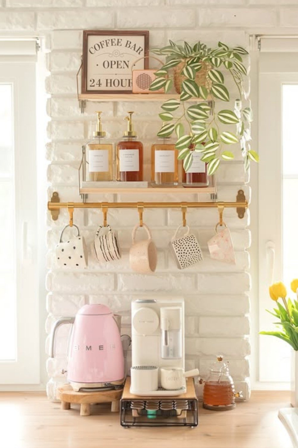 White coffee bar with blush pink coffee machine, mugs, and greenery.