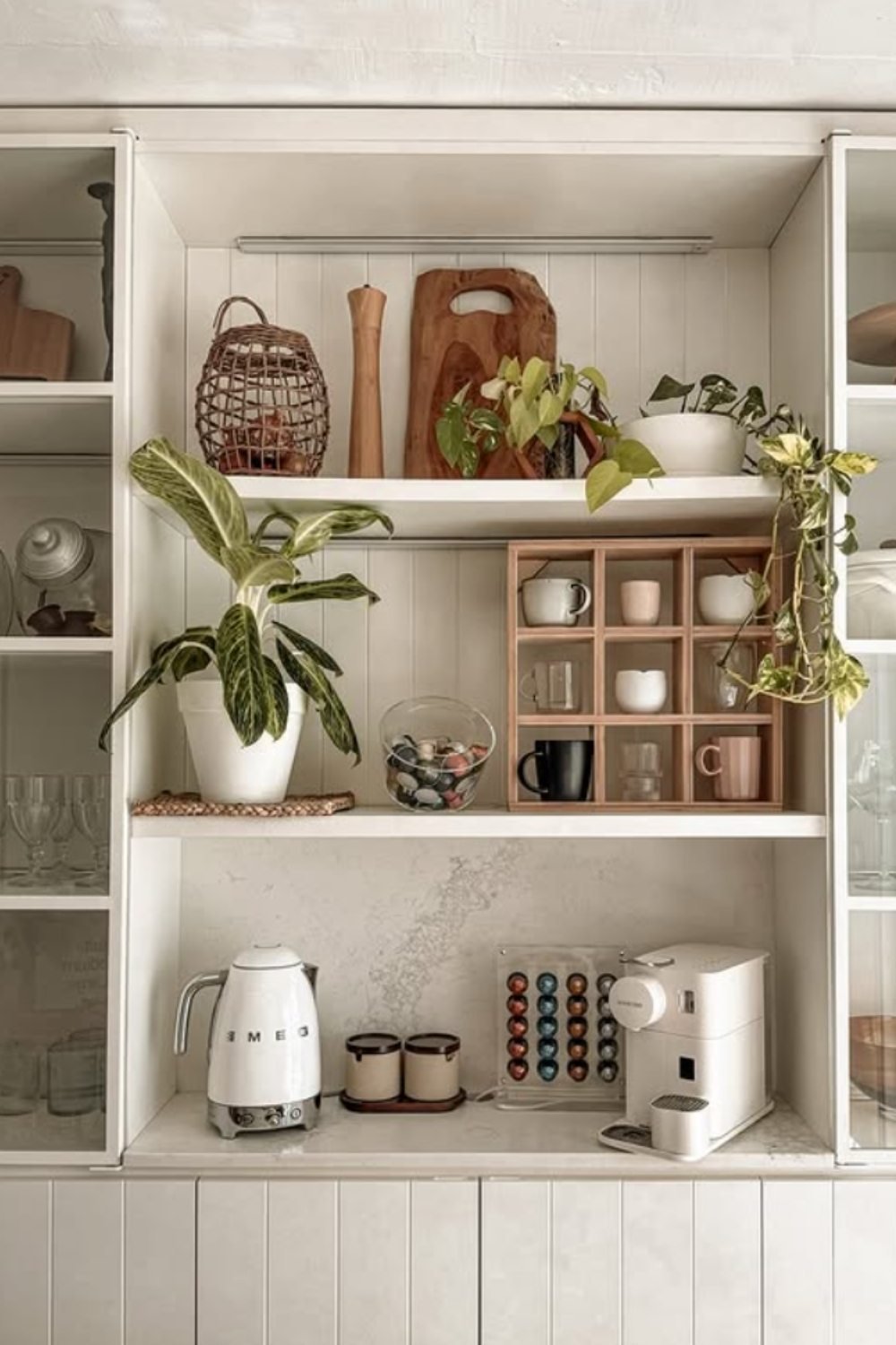 White cubby-style coffee bar with mugs, jars, and greenery accents.