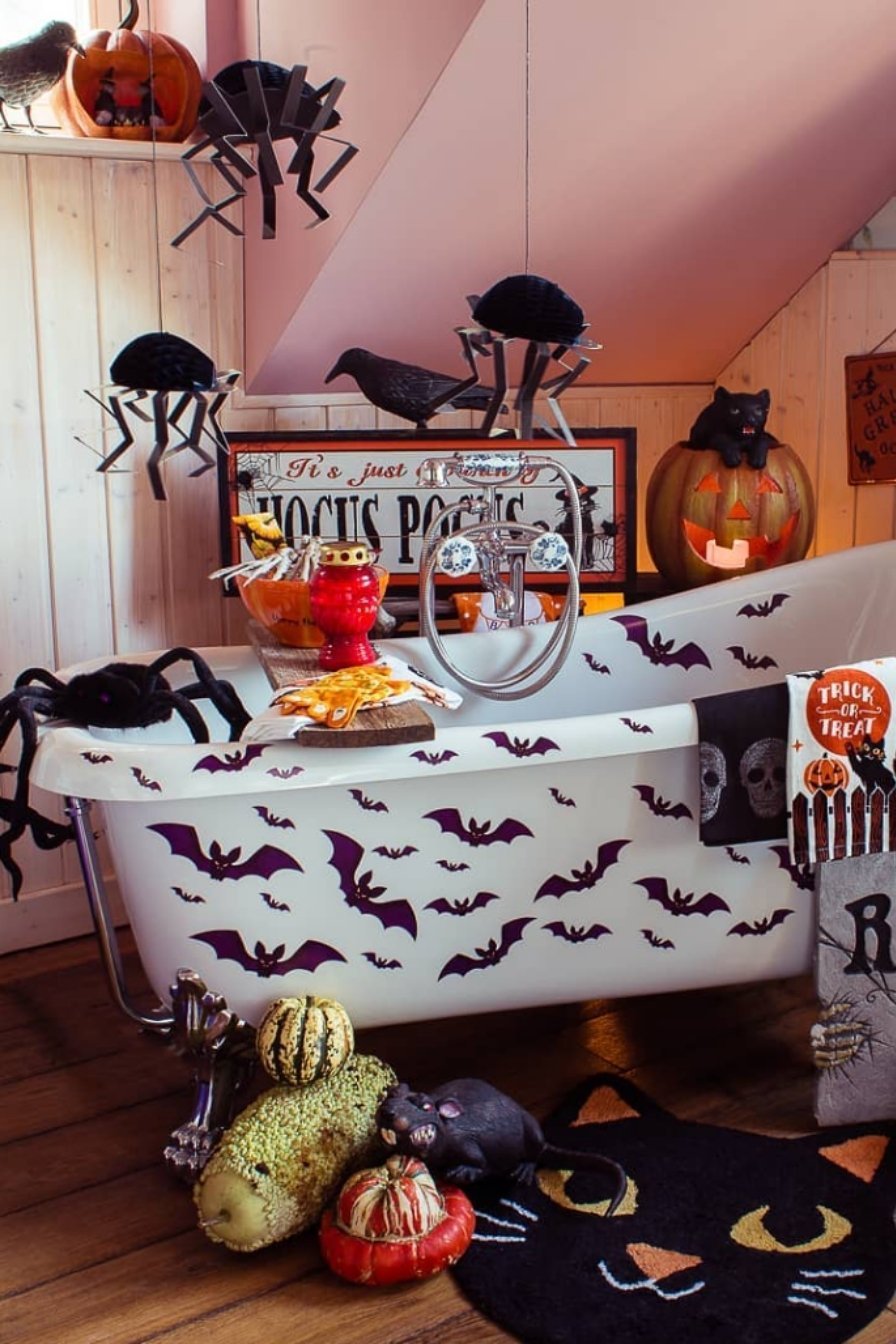 Cozy Halloween bathroom with spider and bat decorations, pumpkins, and themed towels around a white tub.