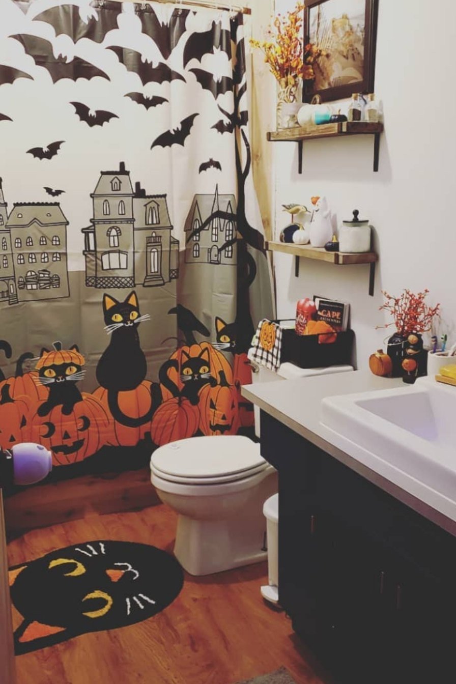 Cute Halloween bathroom with bat and pumpkin wall decals, themed shower curtain, and orange-and-black accents.