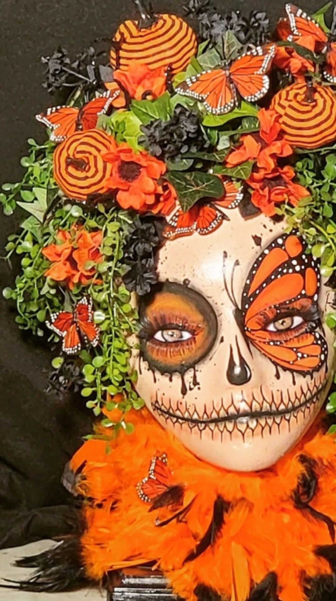 Mannequin head decorated as a sugar skull with flowers, butterflies, and orange feathers