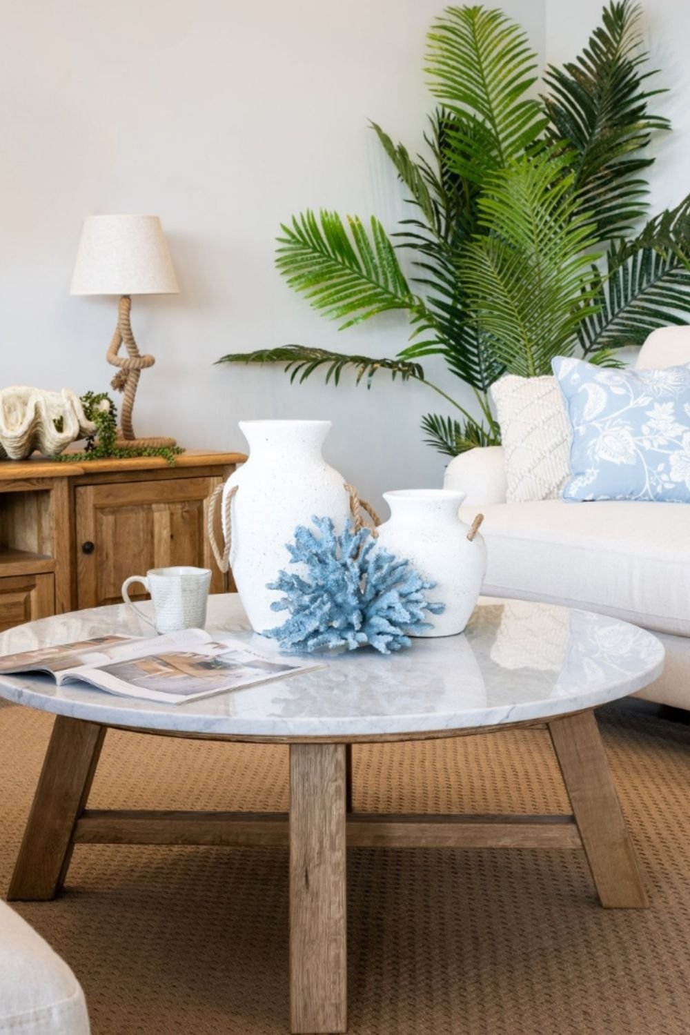 Cozy living room with a round marble coffee table and wooden legs styled with white vases and coastal decor.