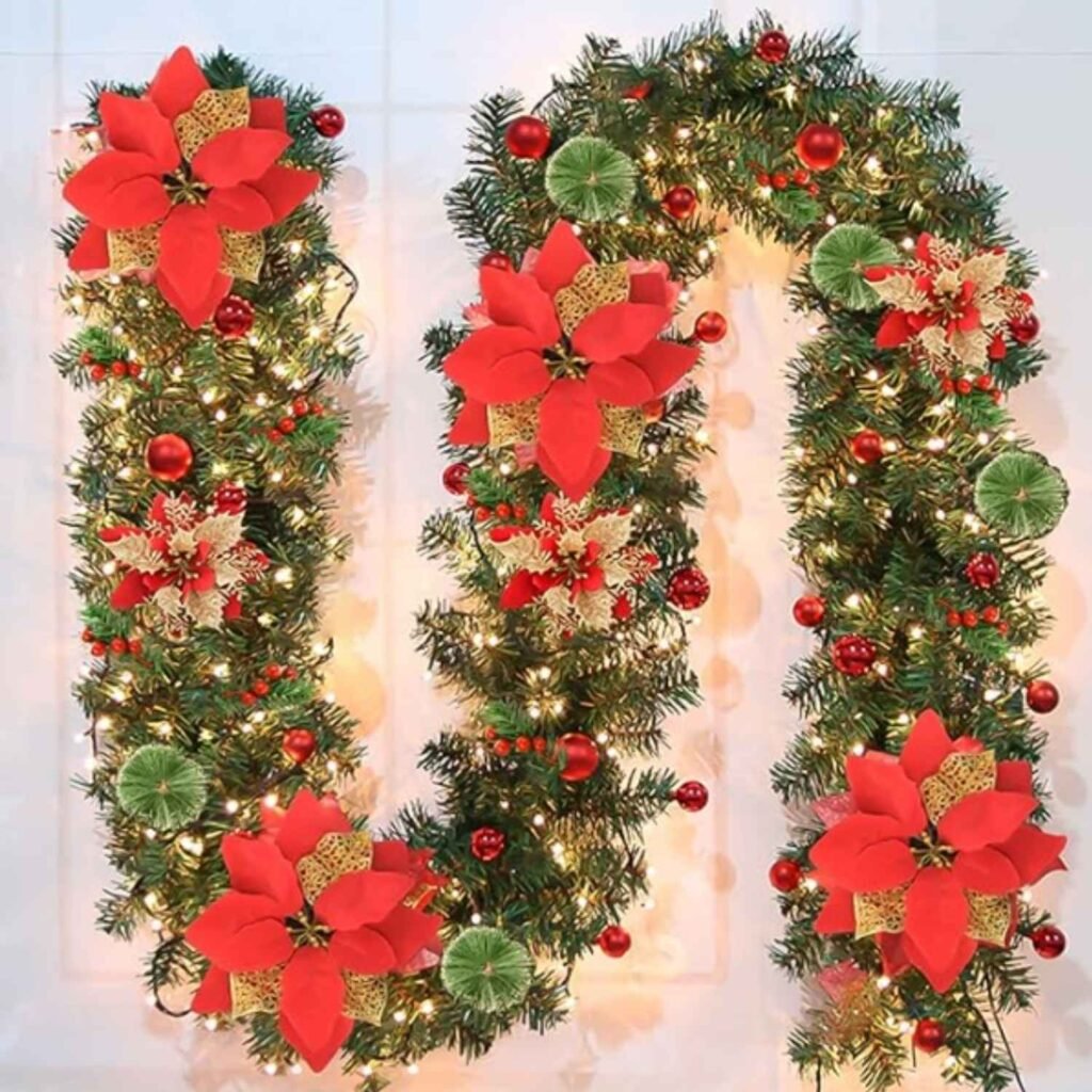 pre-lit Christmas garland with LED lights, red poinsettias, ornaments, berries, and snowy pine branches.