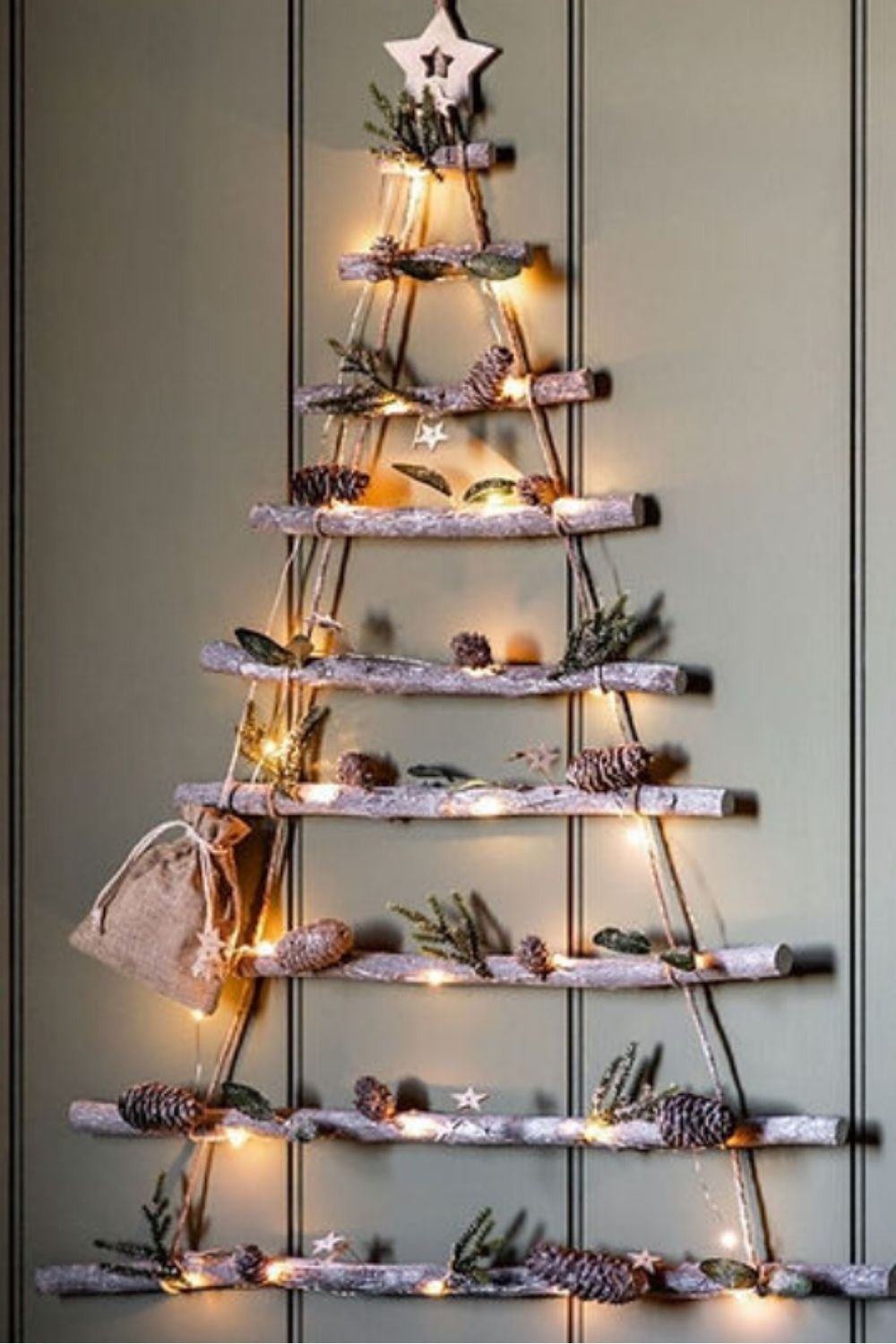 Minimalist wall-mounted Christmas tree made from wooden branches and warm string lights, decorated with pinecones and natural accents.