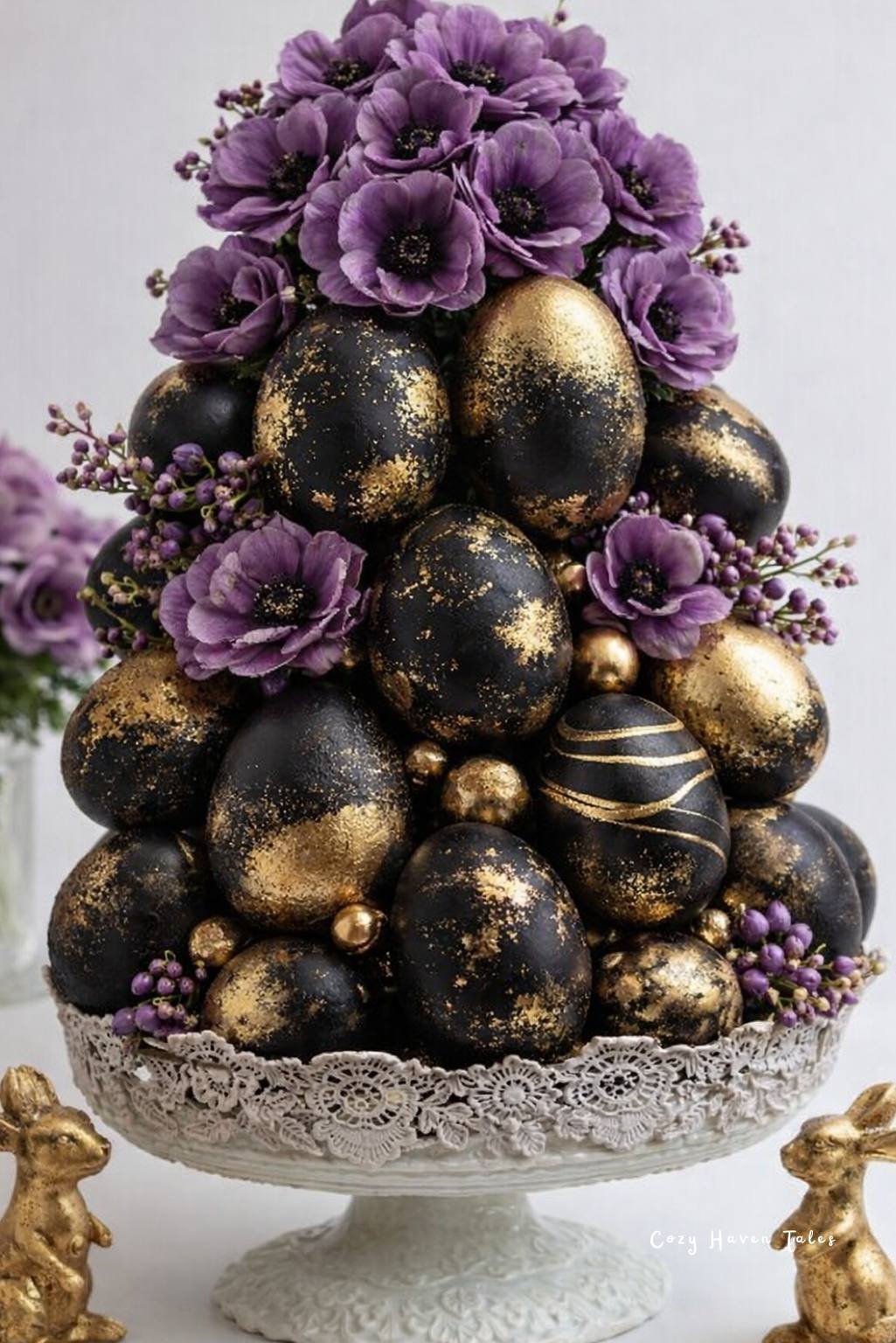 Elegant black and gold egg arrangement topped with purple flowers on a decorative pedestal stand.